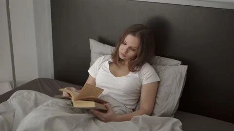 Woman reading a book while lying in bed Stock Footage 132053575