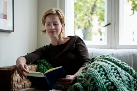 A woman reading a book while reclining on a sofa Stock Photos