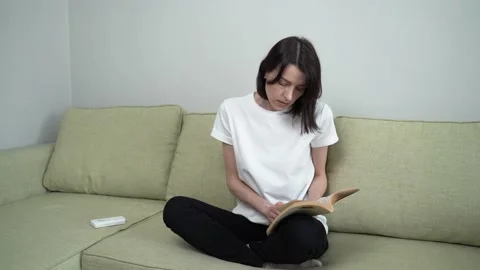 Woman reading a book while sitting on the couch, turns on the cooling air Stock Footage 137855481