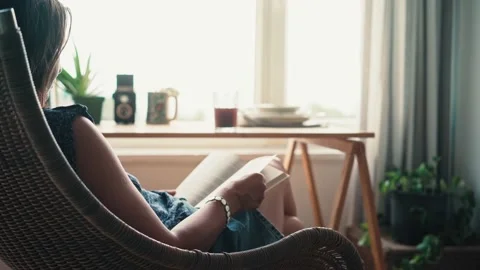 A woman reading a book while sitting in a comfortable wicker chair Stock Footage 200730687