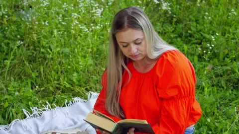 A woman is reading a book while sitting on a blanket in the middle of a field. Video stock 270485710