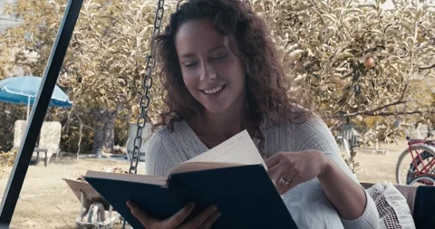 A woman is reading a book while sitting on a swing Stock Footage 283762253