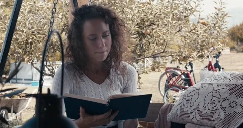 A woman is reading a book while sitting on a swing Stock-Footage 283762482