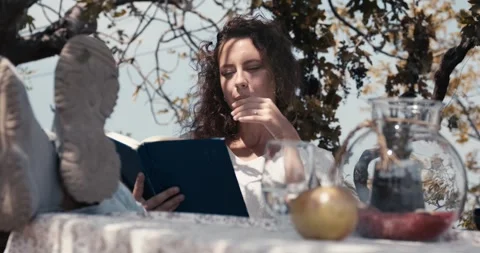 A woman is reading a book while sitting at a table with a glass of water Stock Footage 283763849