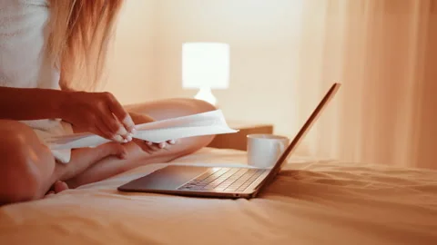 Woman reading documents and typing on laptop in bed Stock Footage 165160564