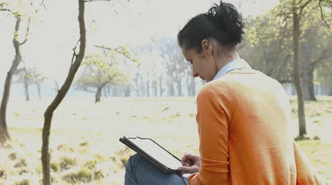 Woman reading guide book map on tablet computer relaxing in a park 스톡 동영상 49009666
