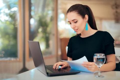 Woman Reading an Important Document while Typing on Laptop Stock Photos