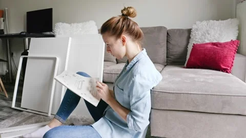 Woman reading instruction before assembling DIY furniture at home. Stock Footage 132587863