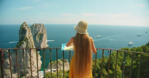 Woman reading a map on a cliffside terrace above Faraglioni rock in Capri in Stock Footage 342683338