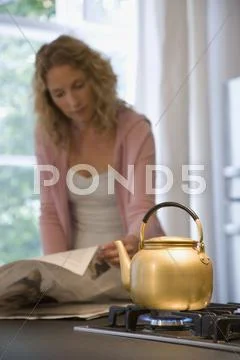 A woman reading the newspaper while waiting for a kettle to boil Stock Photos