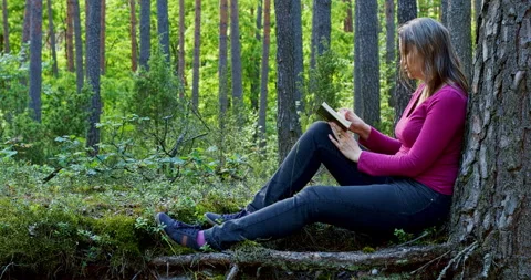 A woman reading a notebook while sitting under a tree in the forest. Stock Footage 279500725