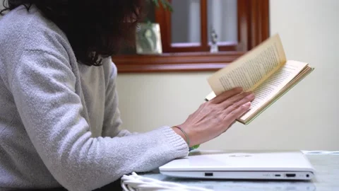 Woman reads a book instead of using computer during quiet day at home Stock Footage 169360234