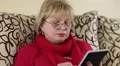 Woman reads a book. Senior woman sits on a sofa and reads electronic book HD Footage