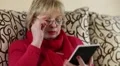 Woman reads a book. Senior woman sits on a sofa and reads electronic book HD Footage