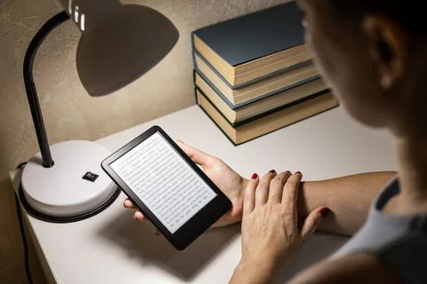 A woman reads an e-reader by the light of a table lamp. Stock Photos