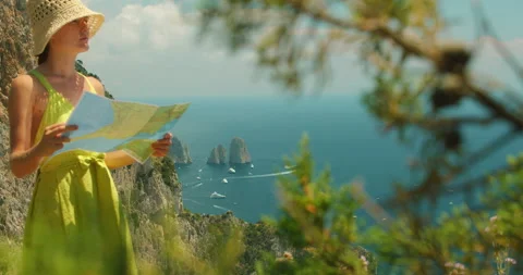Woman reads a map on a cliffside overlooking sea and Faraglioni rock formations Video stock 341366202