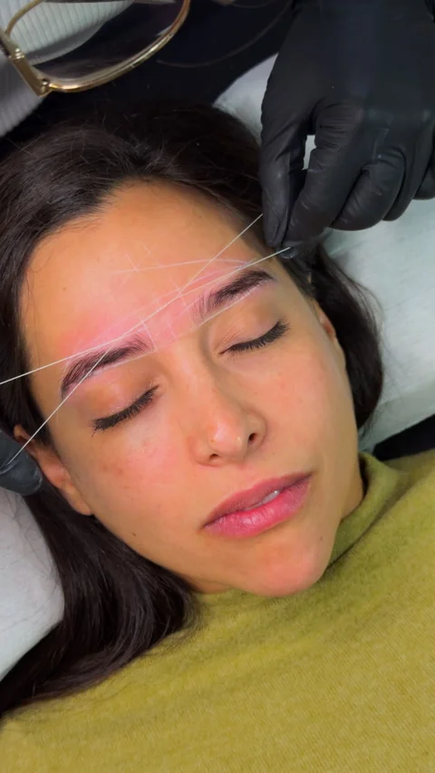 Woman receiving precise eyebrow threading treatment at beauty salon. 库存影片 330986903