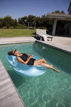 Woman reclining on inflatable float in black swimsuit and sunglasses, holding Stock Photos