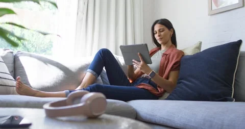 Woman reclining on sofa tapping tablet causing tech UI overlay demoing app and Stock Footage 340613972