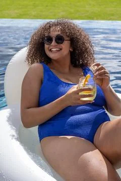 Woman reclining on white float in backyard wearing blue swimsuit and round Stock Photos