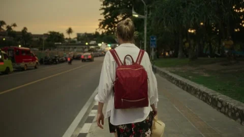A woman with a red backpack is walking down a sidewalk Stock Footage 264810895