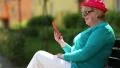 Woman in red cap sits on the bench and communicates via red smartphone HD Footage