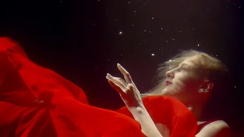 A woman in a red dress dances under the water in a red dress, she tries to touch 库存影片 84606953