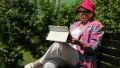 Woman in red hat, jacket, white trousers sits on bench and switches on device HD Footage