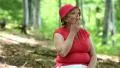 Woman in red hat, T-shirt, sits on log in forest and smoking cigarette HD Footage
