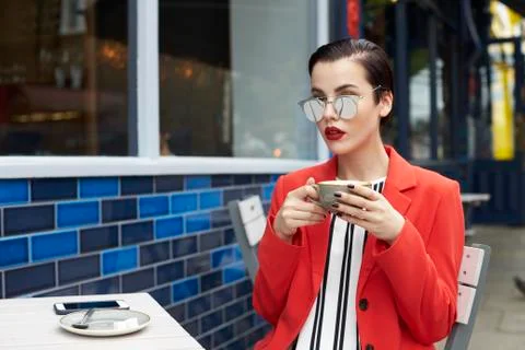 Woman in red jacket sitting outside a cafe, waist up Stock Photos