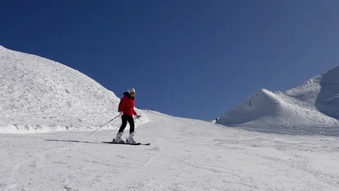 Woman in red jacket skiing down snowy mountain slope on sunny day Stock Footage 327984425