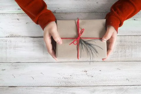 A woman in a red sweater holding a Christmas gift with a red ribbon on a wooden  Stock Photos