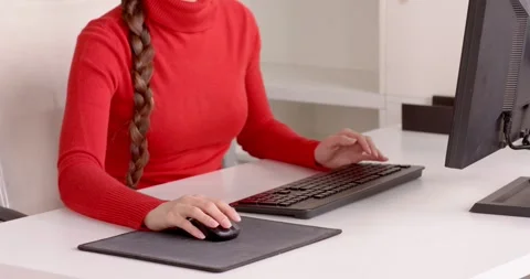Woman in red sweater using computer mouse at office desk, focusing on work Stock Footage 346143789