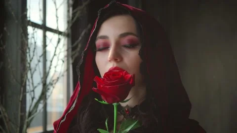 Woman in red velvet vintage hood gently touch rose face. Girl enjoys smell, Stock Footage
