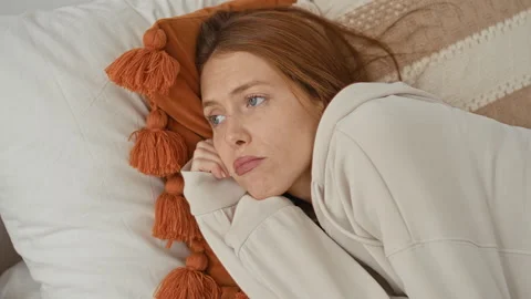 Woman redhead lying on bed with hand to cheek, resting head on tassel pillo.. Stock-Footage 337353576
