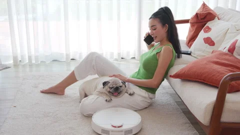 Woman relaxes on a sofa while talking on the phone and petting a pug, with a Stock Footage 300028601
