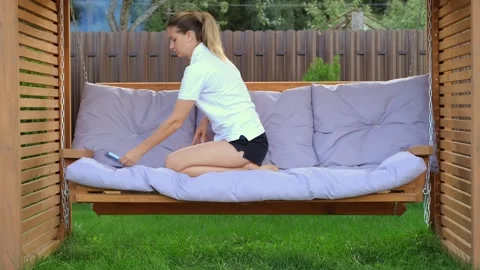 A woman relaxes on a swing in the backyard while looking at her smartphone Stock Footage 250443961