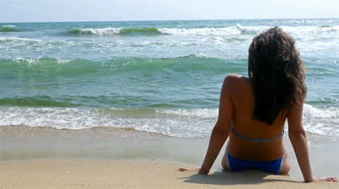 Woman relaxing on the beach, looking at sea water, waves splashing in her body Stock Footage