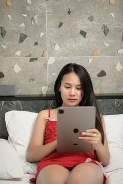 Woman Relaxing on Bed While Using Tablet in Modern Bedroom Setting Stock Photos