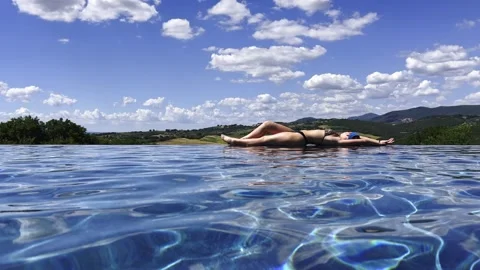 Woman relaxing on edge of infinity pool with countryside view Stock Footage 342344227