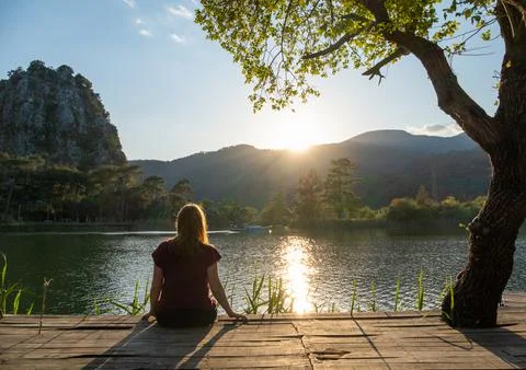 Woman relaxing outdoors near lake or river at sunset Stock Photos