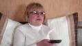 Woman with remote control sits on the bed and switch tv channels HD Footage