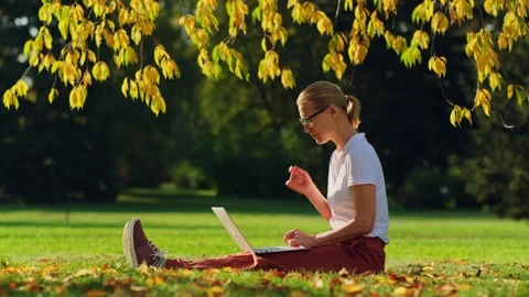 Woman remotely working while sitting on the lawn in autumn park. Видео 251720690