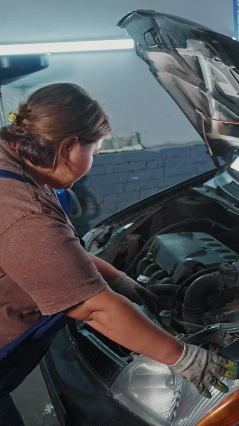Woman repairs car engine in workshop during daylight hours 스톡 동영상 303797927