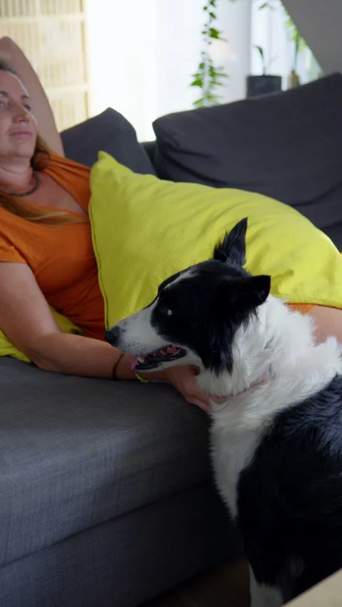 A woman is resting on a sofa whilst her dog lies beside her. 動画素材 346309584