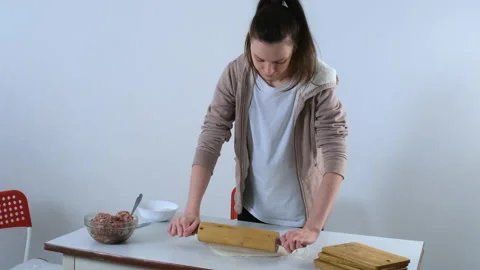 Woman is rolling dough for dumpings using rolling pin on table in kitchen. Stock Footage 153712591