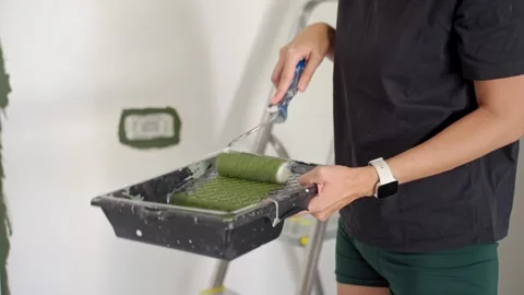 Woman rolling paint roller in tray to cover it with green paint Stock Footage 345006964