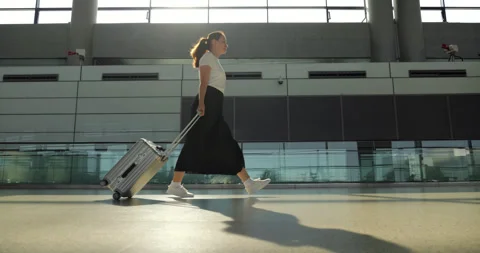 Woman with rolling suitcase walking through empty airport terminal Stock Footage 327653359