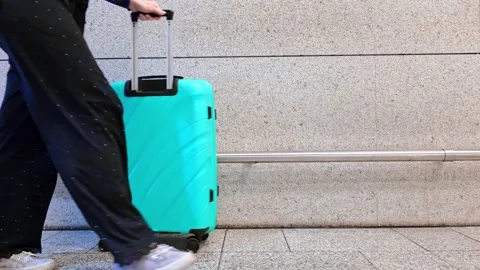 Woman rolling teal hard-shell suitcase across airport floor, travel lifesty.. Stock Footage 338133370