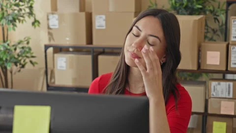 Woman rubbing temple with hand at computer among stacked parcels and boxes .. Stock Footage 337369436